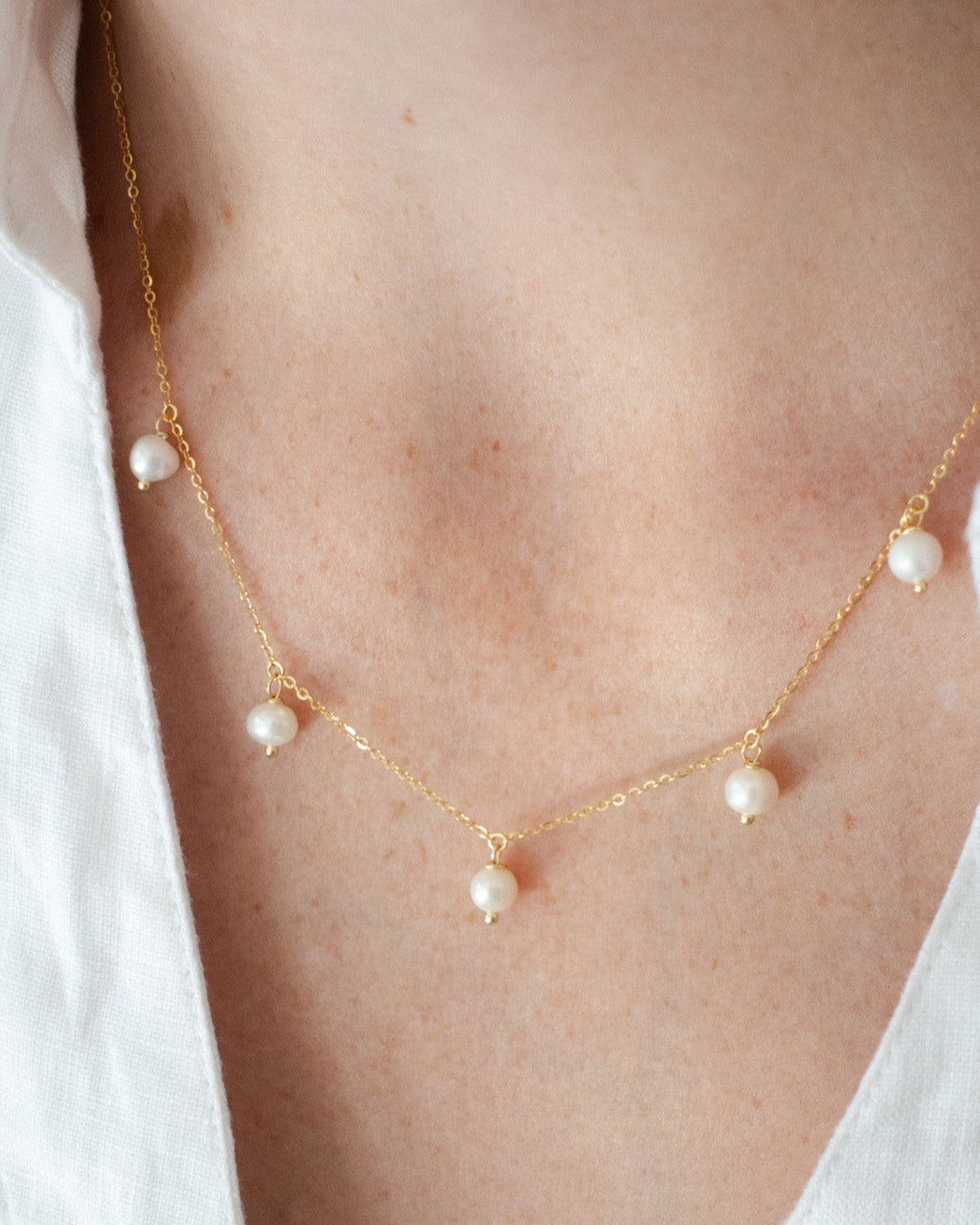Close-up of a sterling silver gold-plated necklace with freshwater pearls on a model wearing a white shirt