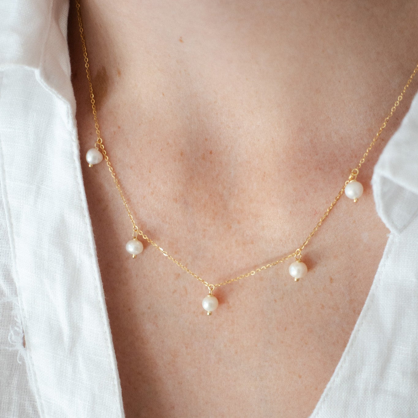 Close-up of a sterling silver gold-plated necklace with freshwater pearls on a model wearing a white shirt